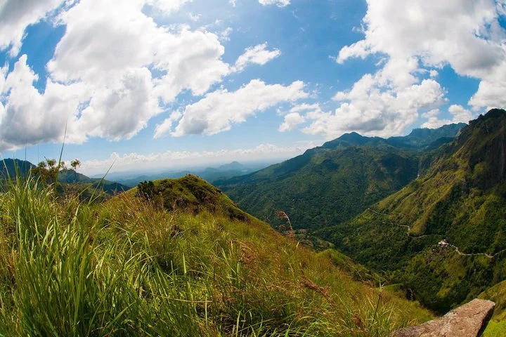 Panoramic view of lush green mountains and a scenic valley beneath a blue sky with clouds